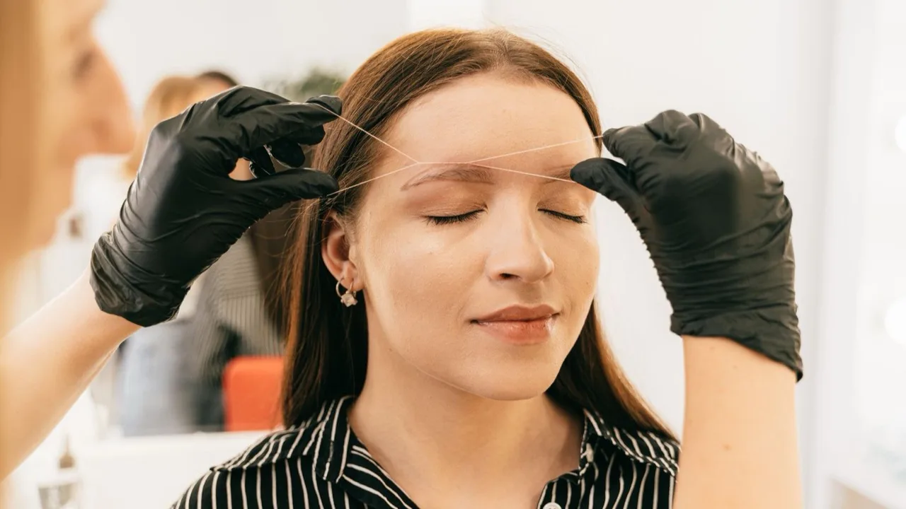 Profesional realizando depilación de cejas con hilo en una cabina de estética